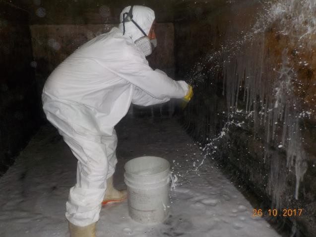 Técnico con traje y mascarilla lavando las paredes de un cárcamo